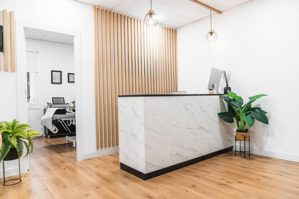 Clean aesthetic medicine clinic reception area with marble counter, wood panel wall and plants